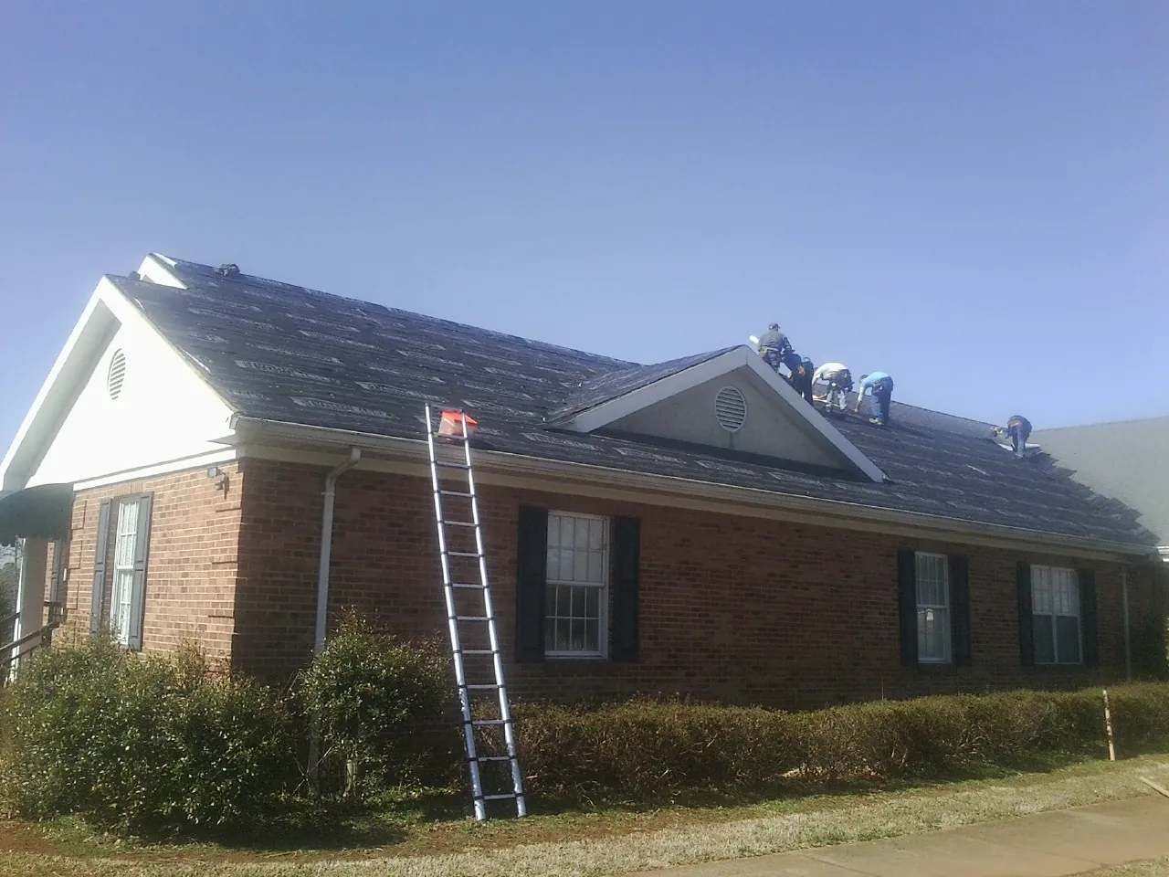 Crew tearing shingles off a brick ranch roof with a ladder set — Emergency Roof Repair work by our crew in East Hanover