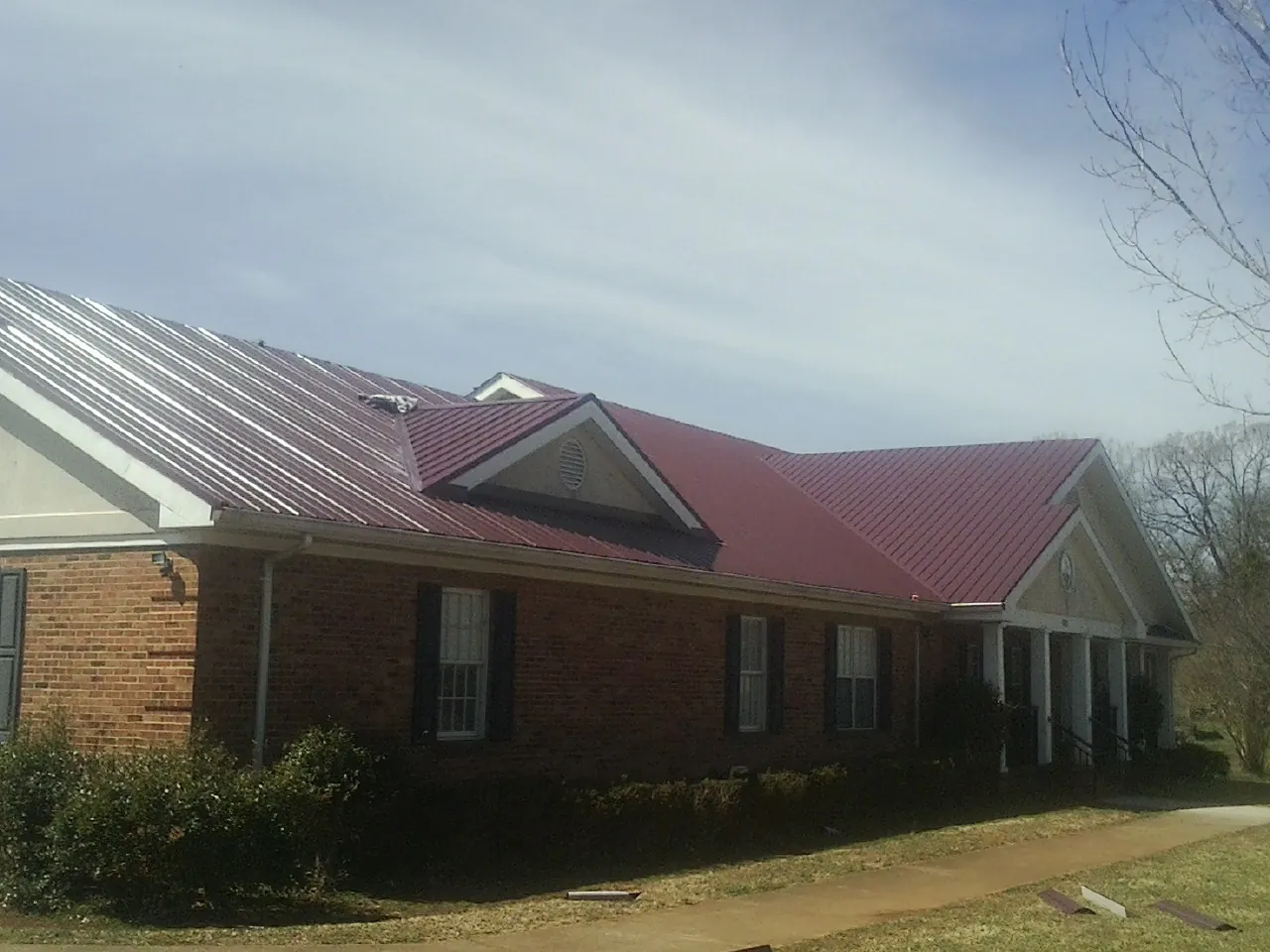 Red metal roof with gabled entries on a long brick building, from a Hail Damage Roof Repair job in East Hanover