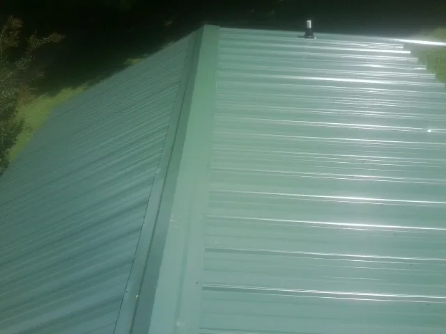 New green metal panels meeting at the ridge of a roof — Flat Roof Repair work by our crew in East Hanover