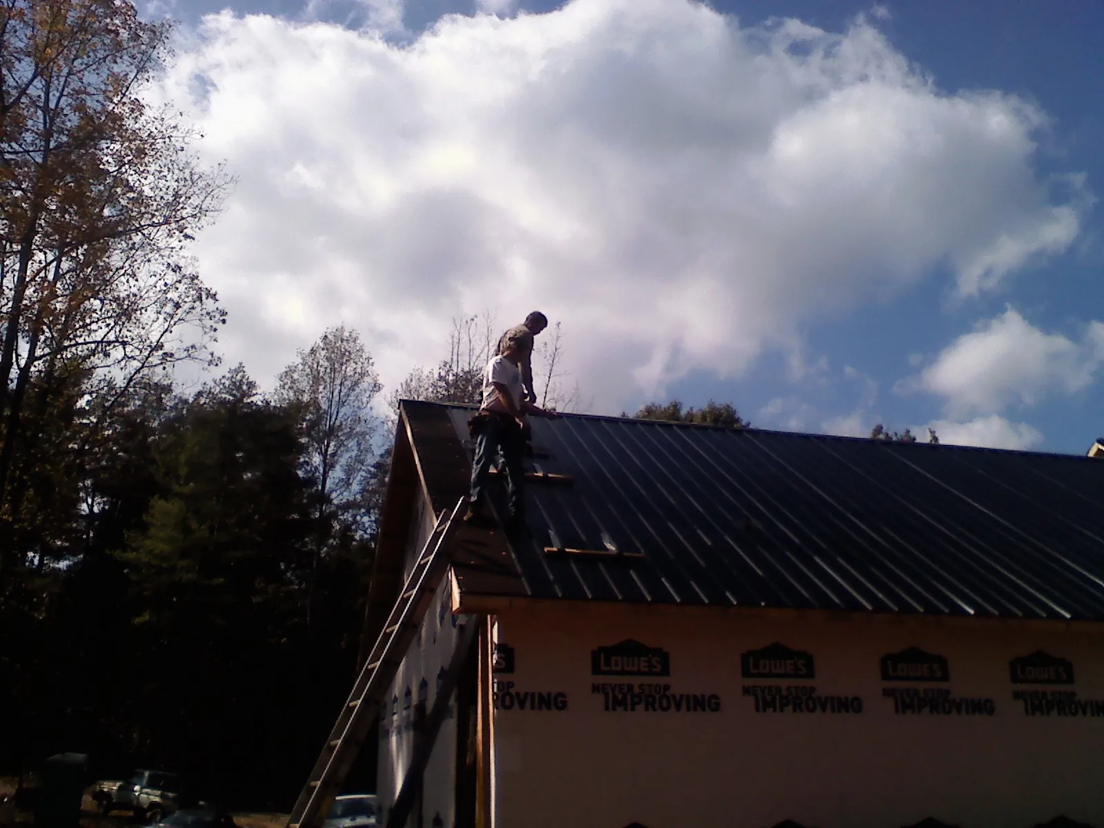 Roofer fastening dark metal panels high against a cloudy sky, from a Roof Inspection job in East Hanover