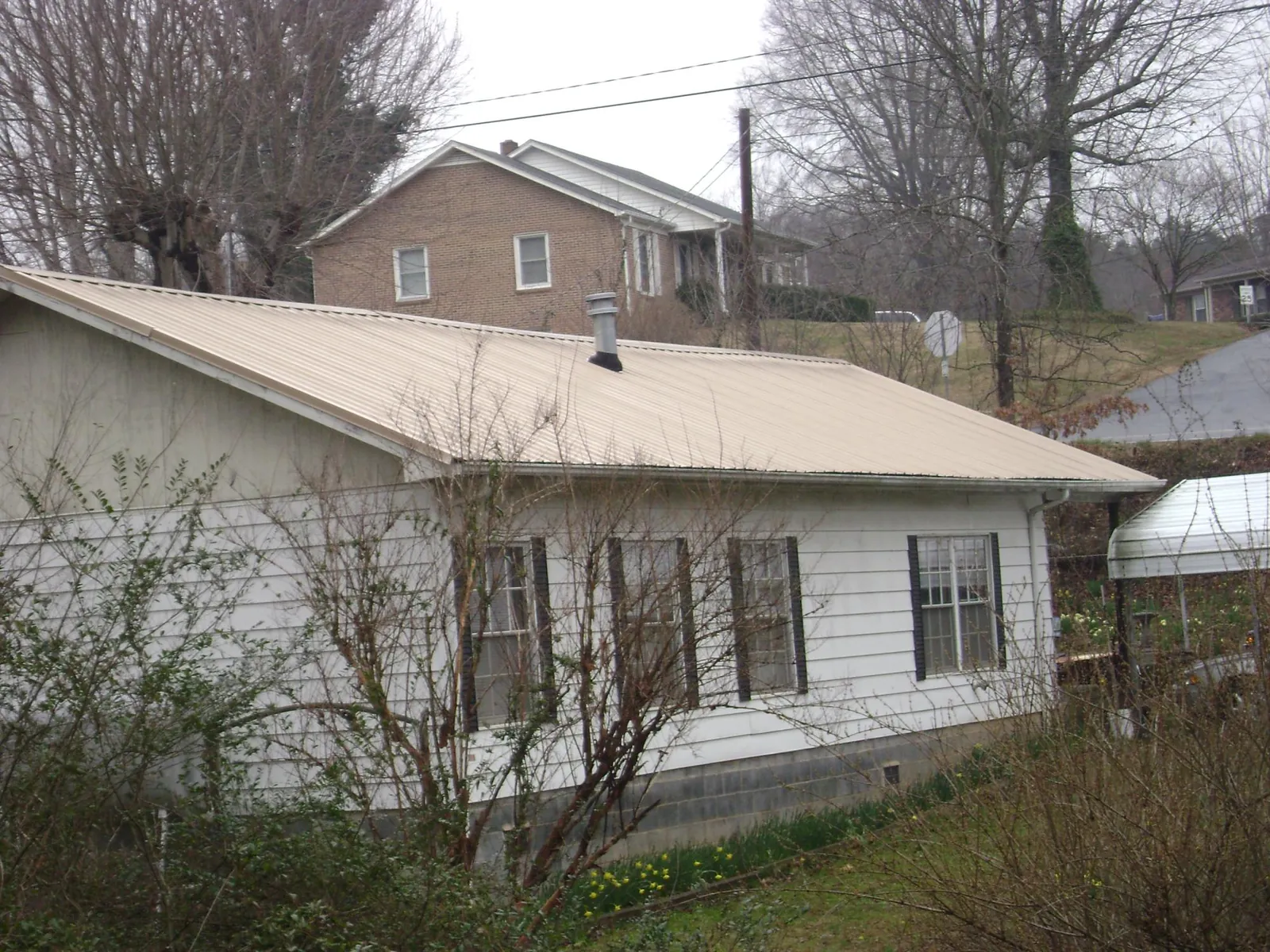 Tan metal roof on a white sided house set into a hillside — Commercial Roofing by Roofing Brothers in East Hanover